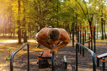 Athletic young Caucasian man doing push ups on parallel bars