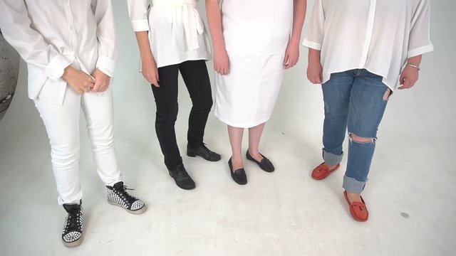 Four people dressed in jeans, dress, whete pants standing on a floor. isolated over white background