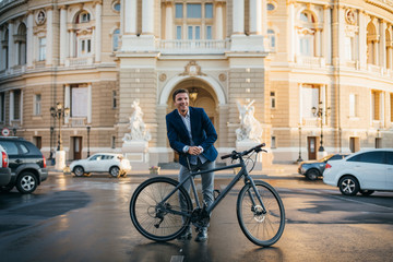Fototapeta premium Portrait of handsome young man with his bicycle on the street in city center during sunrise