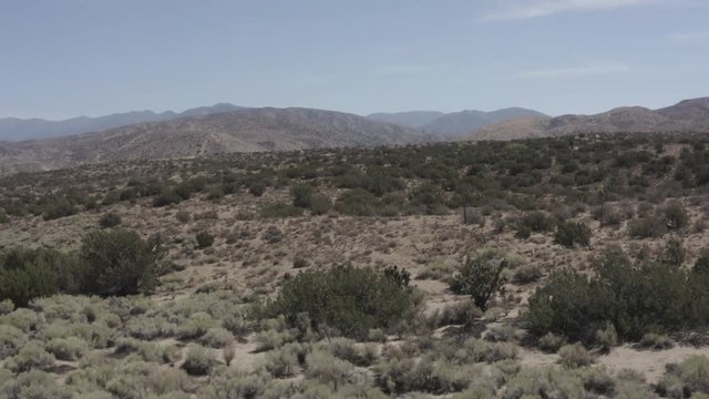 Aerial pullback shot of a barren desert land with some small shrubs.