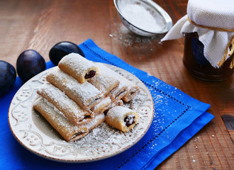 Plate of biscuit rolls filled with plum jam with powdered sugar over blue napkin