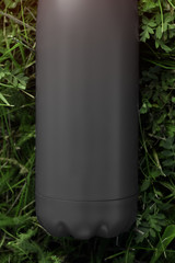 Stainless thermos bottle for water, black color. Isolated on green grass background with sunlight effect.