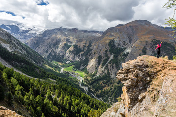 Girl on summit of mountain peak with a valley covered with pine forest at background. Gran Paradiso National Park - Cogne - Aosta Valley