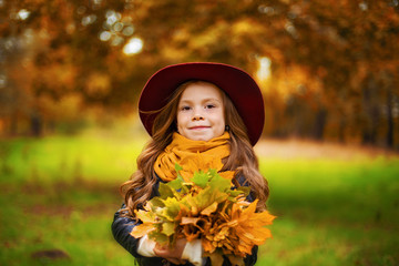 Portrait of a smiling young girl who is holding in her hand a bouquet of autumn maple leaves in the park