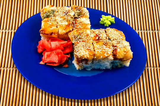 Sushi with salmon, avocado, ginger, wasab on blue plate on yellow mat background.