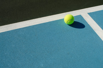 Tennis ball rests on blue tennis court - Powered by Adobe