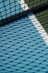 Tennis court net casts shadow on blue ground