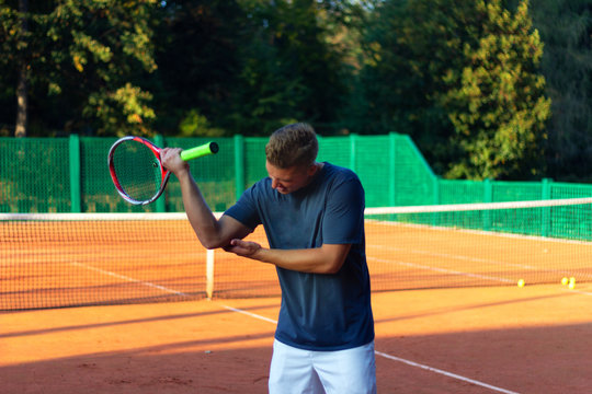 Handsome man on tennis court. Young tennis player. Pain in the elbow
