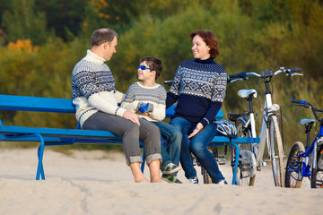 Young family of three having rest on bench during their bike riding on beach