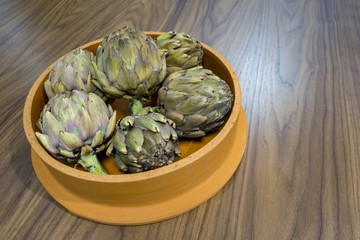 dried decretive artichokes on a clay orange ceramic bowl on a wood table