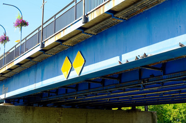 Ailing blue rusty pedestrian bridge over a river in the city with doves and flowers to illustrate poor infrastructure in Germany