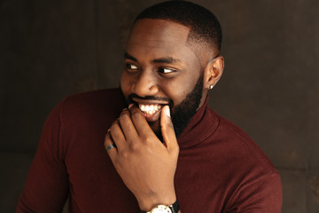 Man portrait. Style. Handsome Afro American guy in wine-colored sweatshirt is smiling, on a dark...