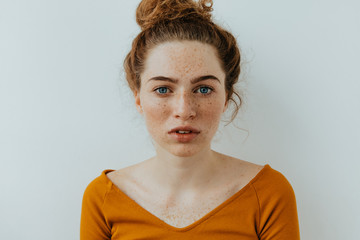 Woman portrait. Style. Beautiful blue eyed girl with freckles is looking at camera, on a white...