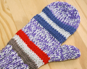 Bright and colorful handmade knitted mitten in red, purple, blue and white stripes 
