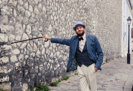 Portrait of hipster man in vintage suit holding wall with walking stick