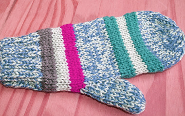 Bright and colorful handmade knitted mitten in blue, white, pink and green stripes
