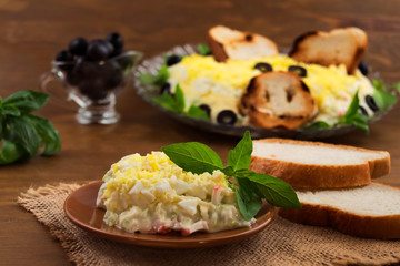 A portion of a cold snack on a plate with basil  leaves, toast, pickled olives.