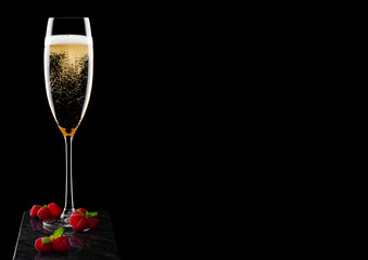 Elegant glass of yellow champagne with raspberries with mint leaf on black marble board on black background. Space for text