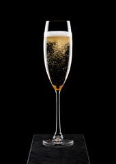 Elegant glass of yellow champagne with bubbles on black marble board on black background.