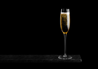Elegant glass of yellow champagne with bubbles on black marble board on black background. Space for...