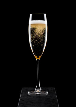 Elegant glass of yellow champagne with bubbles on black marble board on black background.