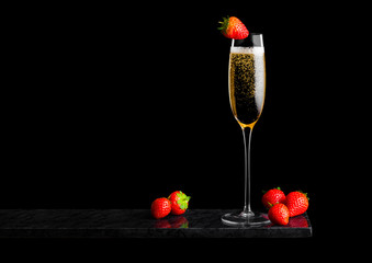 Elegant glass of yellow champagne with strawberry on top and fresh berries on black marble board on black background. Space for text © DenisMArt