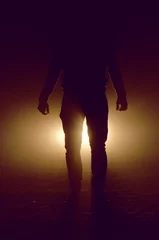 Gordijnen mysterious silhouette of unknown man standing in darkness illuminated from behind by spotlight © javiemebravo
