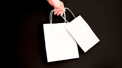 Female hand holding blank white paper bag isolated on black background