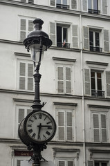 Fototapeta na wymiar Clock and streetlight old and typical of Paris in Montmartre with a French flag at a window