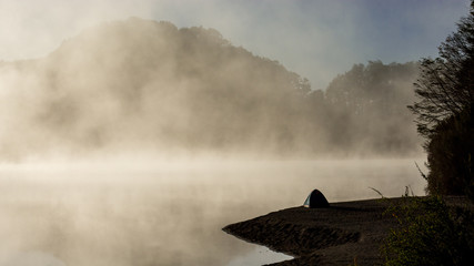 Isolated camping tent with a foggy background covered in early morning low clouds, next to a lake in a remote natural site, Villa la Angostura, Argentina