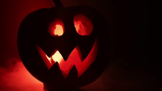 Halloween pumpkin smile and scrary eyes for party night. Close up view of scary Halloween pumpkin with eyes glowing inside at black background. Selective focus