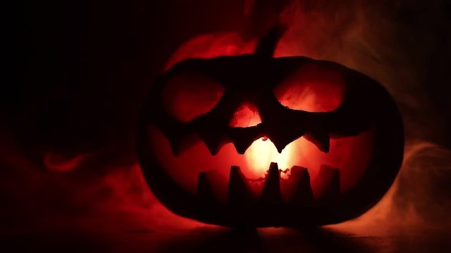 Halloween pumpkin smile and scrary eyes for party night. Close up view of scary Halloween pumpkin with eyes glowing inside at black background. Selective focus