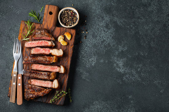 Sliced steak Striploin, grilled with pepper, garlic, salt and thyme served on a wooden chopping Board on a dark stone background. Top view with copy space