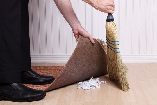 Unrecognizable man sweeping dirt under a rug