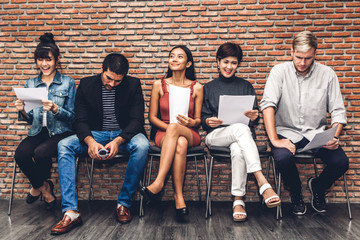 Group of business people holding paper while sitting on chair waiting for job interview against brick background