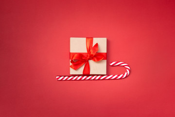 Christmas sledge - a gift box over candy cane on a red background. Abstract christmas concept.