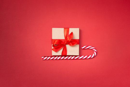 Christmas sledge - a gift box over candy cane on a red background. Abstract christmas concept.