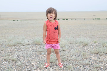 Little girl screaming in big landscape environment. Child emotionally saying loudly something, singing a song with expression