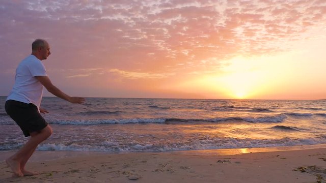 Athletic man practicing asian martial arts Tai Chi at sunset over the sea