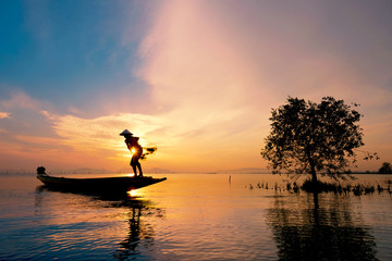 Naklejka na ściany i meble Fisherman on boat catching fish with sunrise