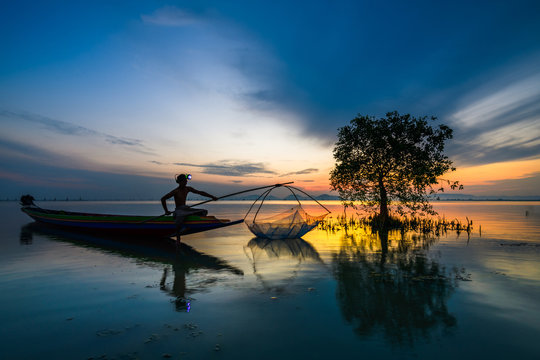 Fisherman on boat catching fish with sunrise