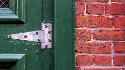 Close up of an old slightly rusty green door hinge attached brick wall.