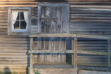Rustic entrance to old wood cabin with unfinished clapboard siding, a window, a door, and a stoop with ramp and handrail.