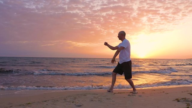 Athletic man practicing Tai Chi asian martial arts on sea beach in the morning