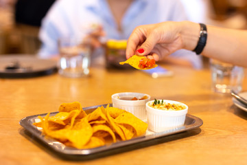 Womans hand with red color nail having a tortilla chip bruschetta sauce at lunch time with friend.