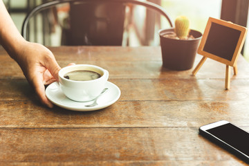 Waiter serving cup of coffee in with cell phone on cafe table.