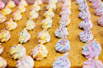 Many colorful rainbow sugar confectionery meringues ready to serve on tray in kitchen.