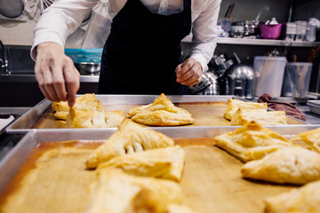 Close-up of chef in apron baking and making many handmade breads on tray freshly baked from over in kitchen for commercial bakery shop.