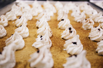 White whipped cream of meringues with chocolate chips and cocoa on top on bakery tray in kitchen.