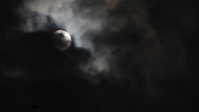 Black clouds passing in front of the moon in the night sky. Outdoor at nighttime..